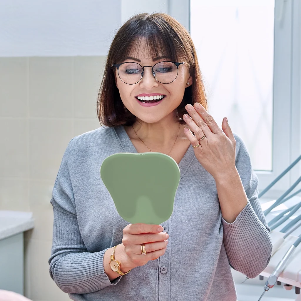 happy woman dentist patient with mirror in hands looking at her teeth